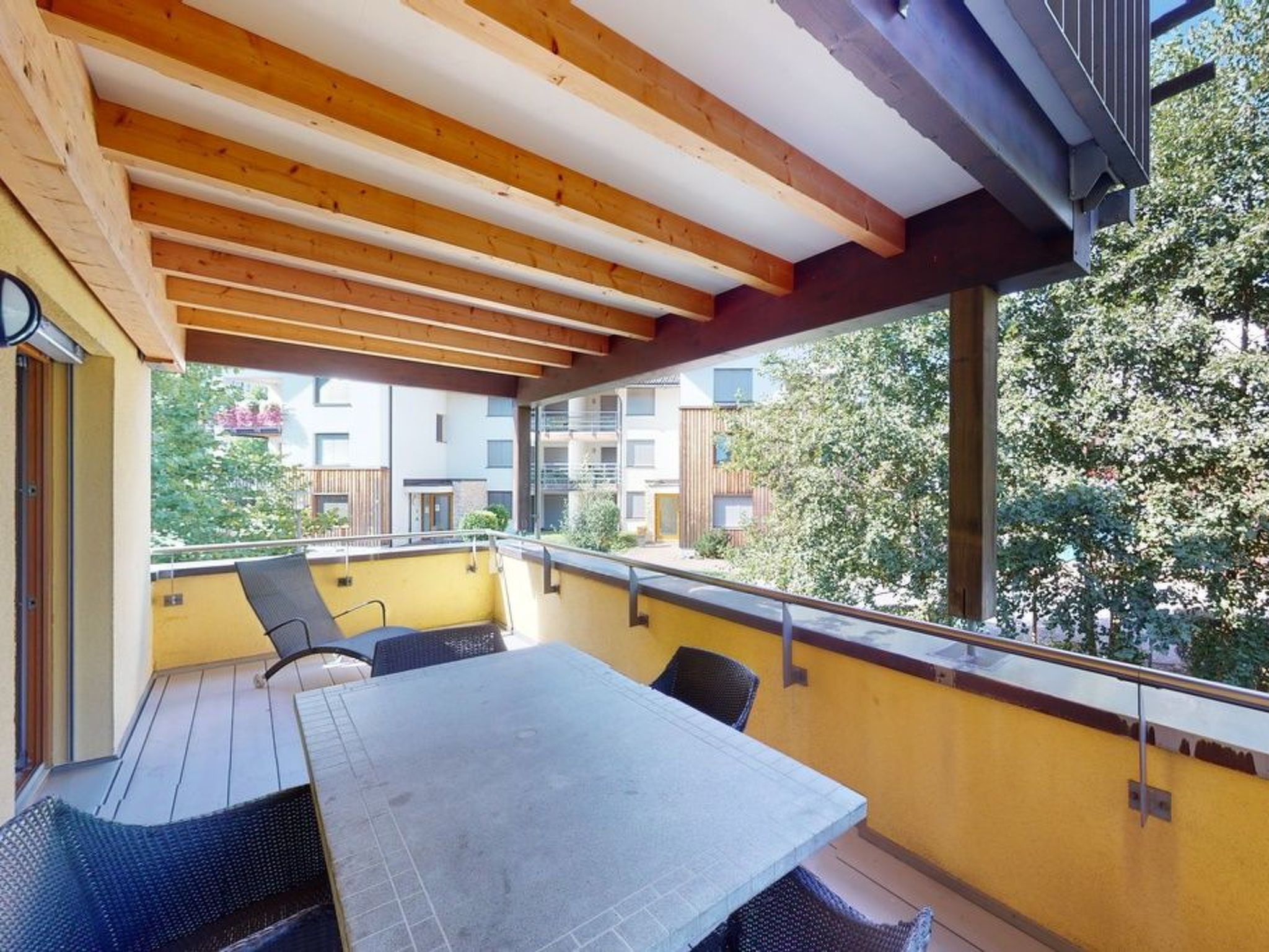 Un balcon couvert, agrémenté d’une table et de chaises, donnant sur un quartier résidentiel.