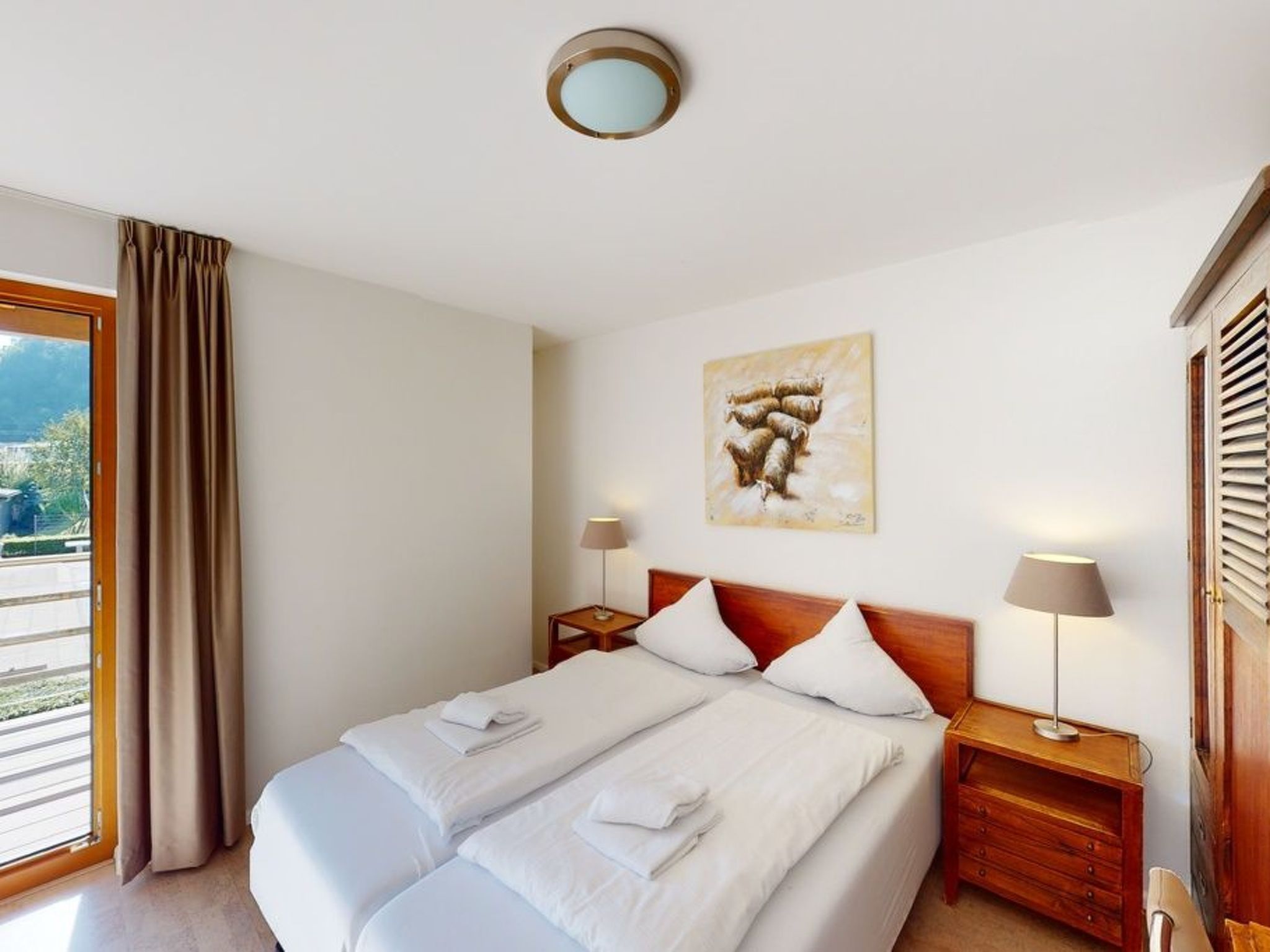 Ein Hotelzimmer mit einem Bett, zwei Nachttischen, einer Lampe, einem Gemälde und einem Fenster mit Vorhängen.