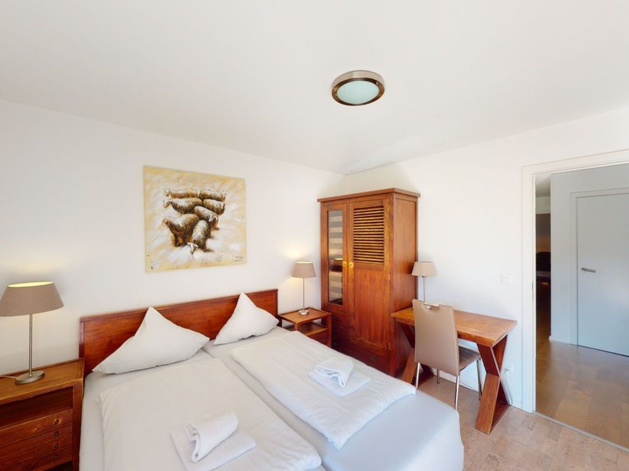 Habitación de hotel con cama, mesitas de noche, escritorio, silla, armario y un cuadro en la pared.