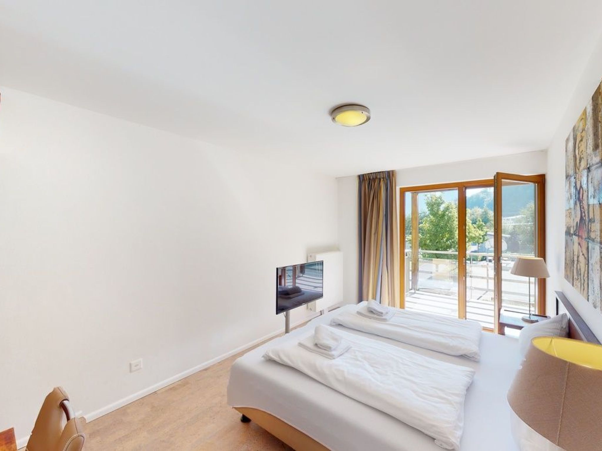 Quarto de hotel com cama, escrivaninha, televisão e uma grande janela com vista.