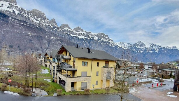 Un edificio amarillo con balcón, rodeado de montañas nevadas.