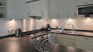 Una cocina moderna con gabinetes blancos, un microondas Bosch, electrodomésticos de acero inoxidable y un horno empotrado.