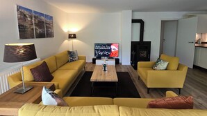 Una sala de estar con dos sofás amarillos, una mesa de centro, un televisor, una chimenea y una lámpara.