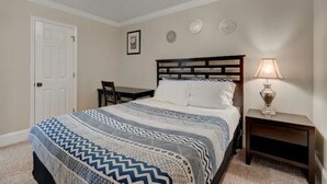 Un dormitorio con cama, mesita de noche, lámpara, silla y puerta.
