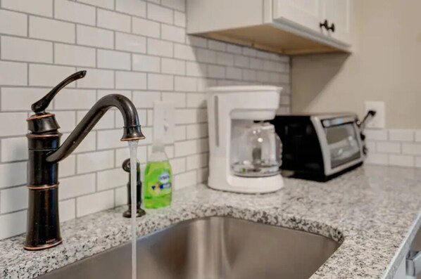 A kitchen with a stainless steel sink, a black faucet, a white coffee maker, and a toaster on the countertop.