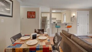 Un comedor con una mesa dispuesta para cuatro personas, un sofá y una cocina al fondo.
