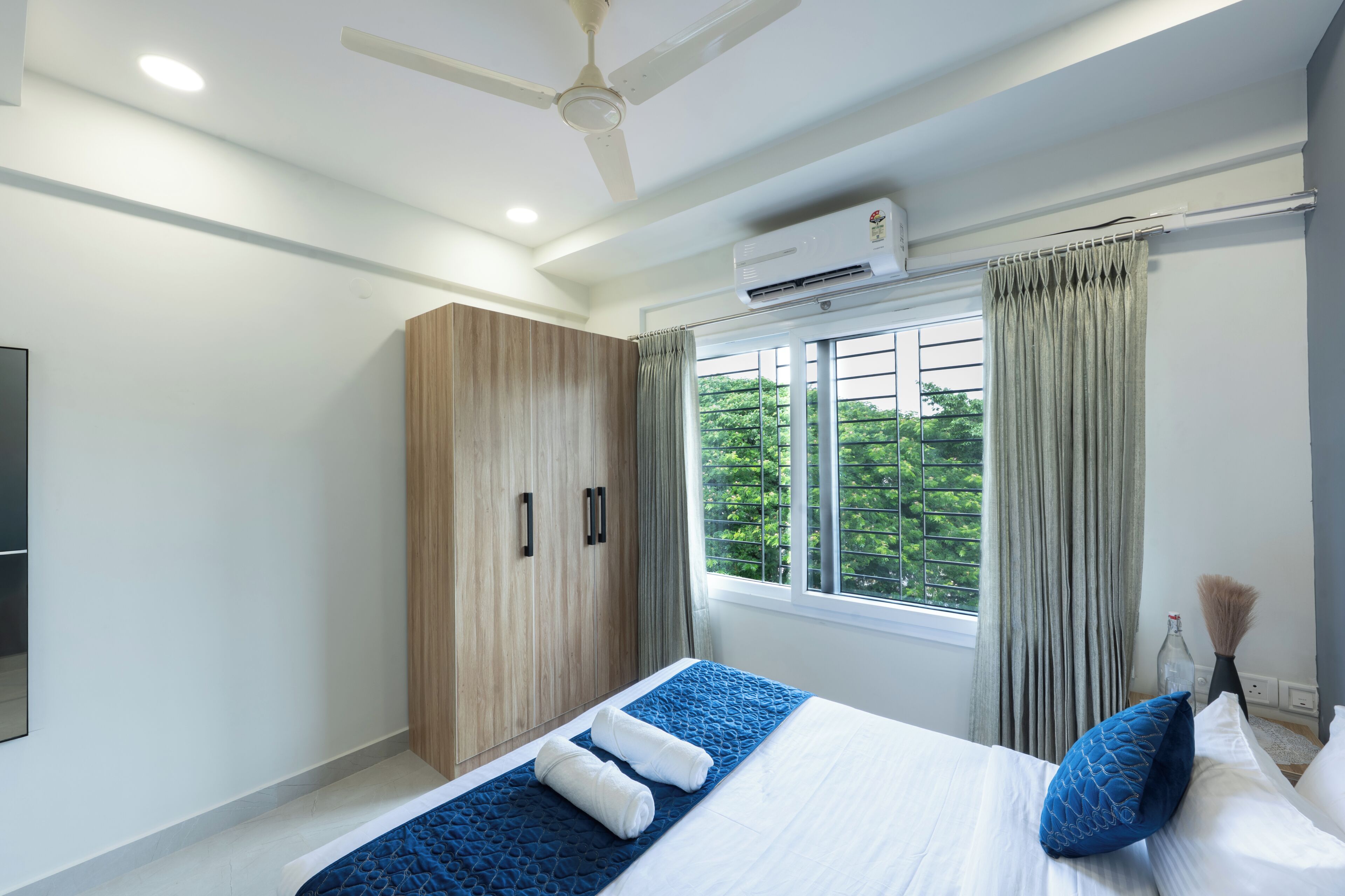 Habitación de hotel moderna con cama, armario, equipo de aire acondicionado y ventana con cortinas.