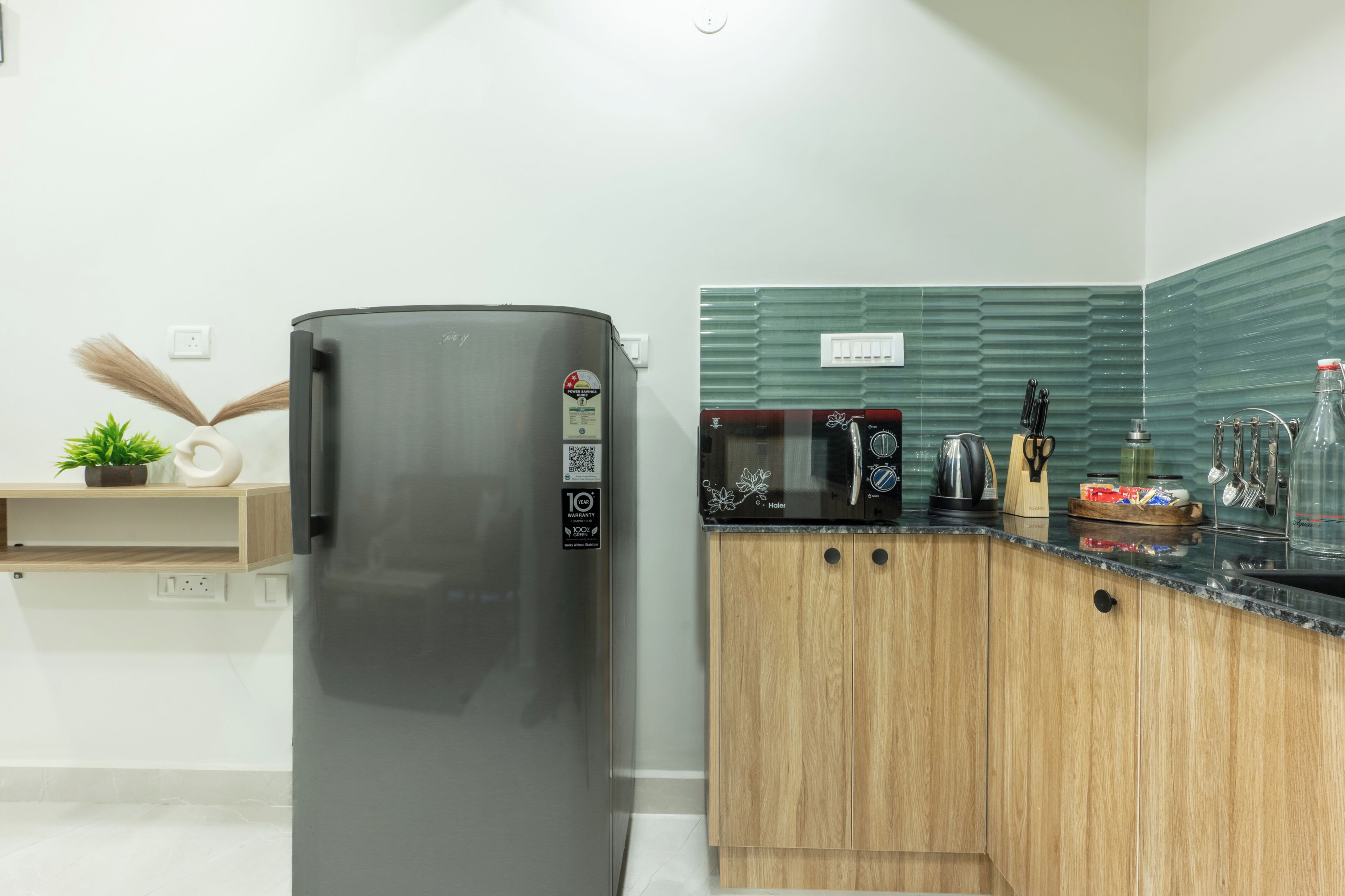 Una cocina moderna con un refrigerador de acero inoxidable, armarios de madera, un microondas y una tetera sobre la encimera.