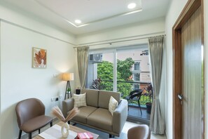 A modern living room with a sofa, chairs, a table, and a large window with curtains. - Buteak Suites Koramangala Club Rd (Bengaluru)
