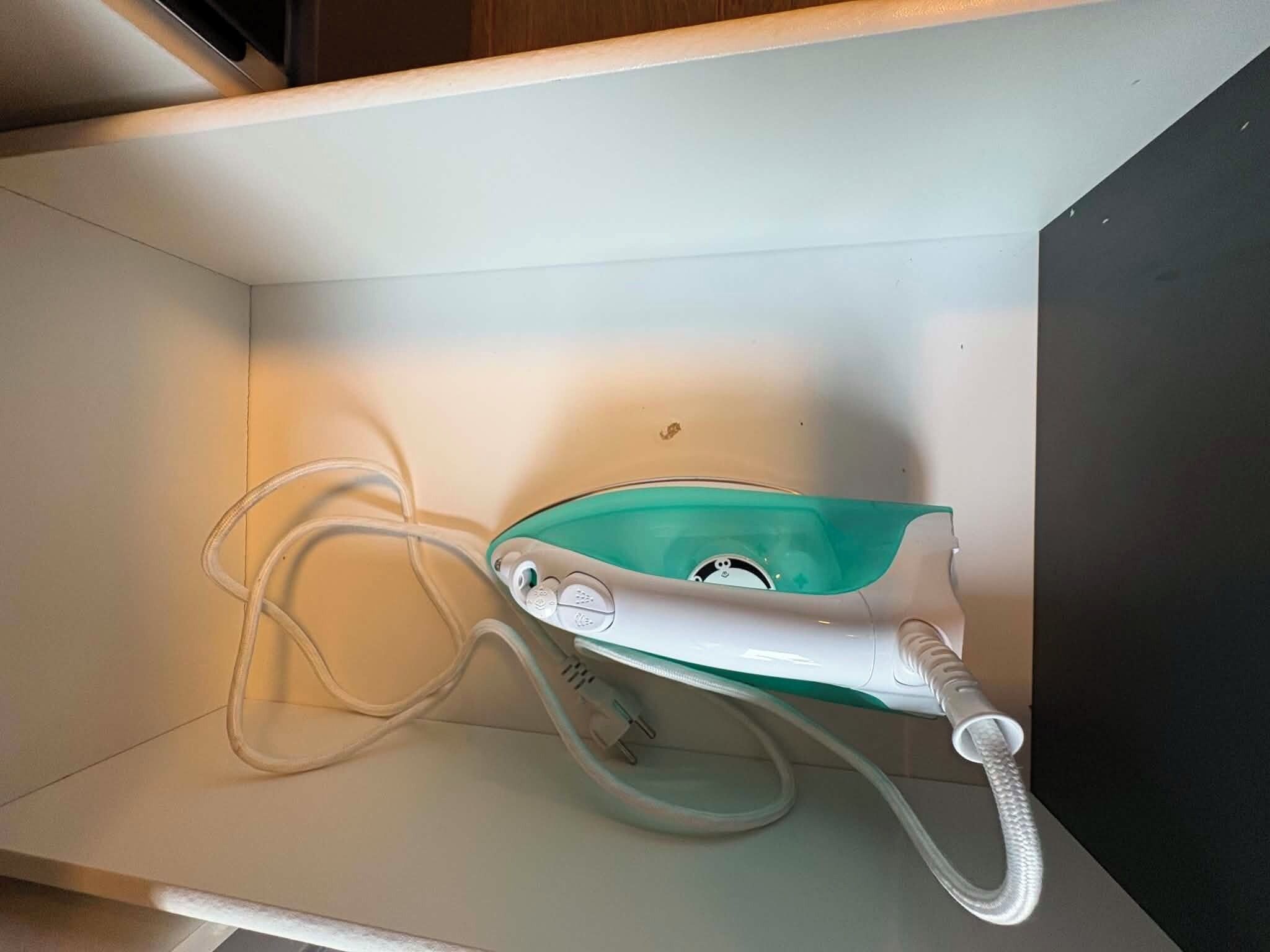 A hair dryer with a cord plugged in, placed on a white surface.