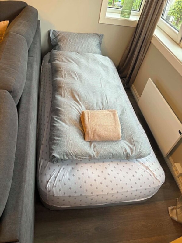 A small, narrow bed with a pillow and a blanket, positioned next to a gray sofa. - Notodden Sentrum Apartment NO 14 (Telemark)