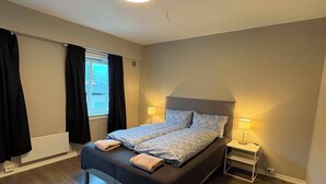 A bedroom with a bed, two bedside lamps, a window with curtains, and a ceiling light. - Notodden Sentrum Apartment NO 14 (Telemark)