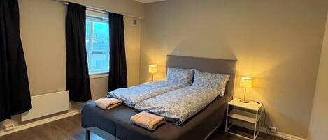 A bedroom with a bed, two bedside lamps, a window with curtains, and a ceiling light.