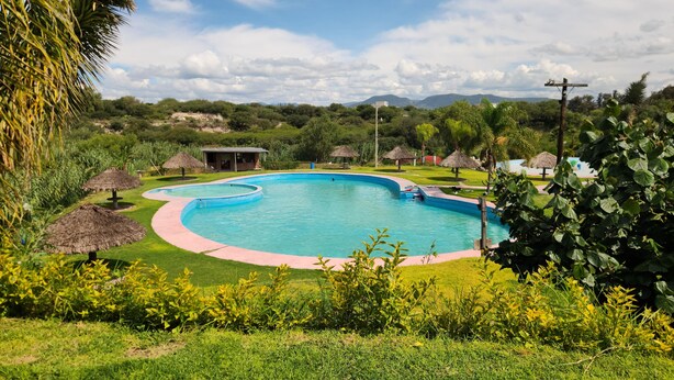 Una piscina de disseny corbat, envoltada d'herba i plantes tropicals, amb vista a les muntanyes al fons.