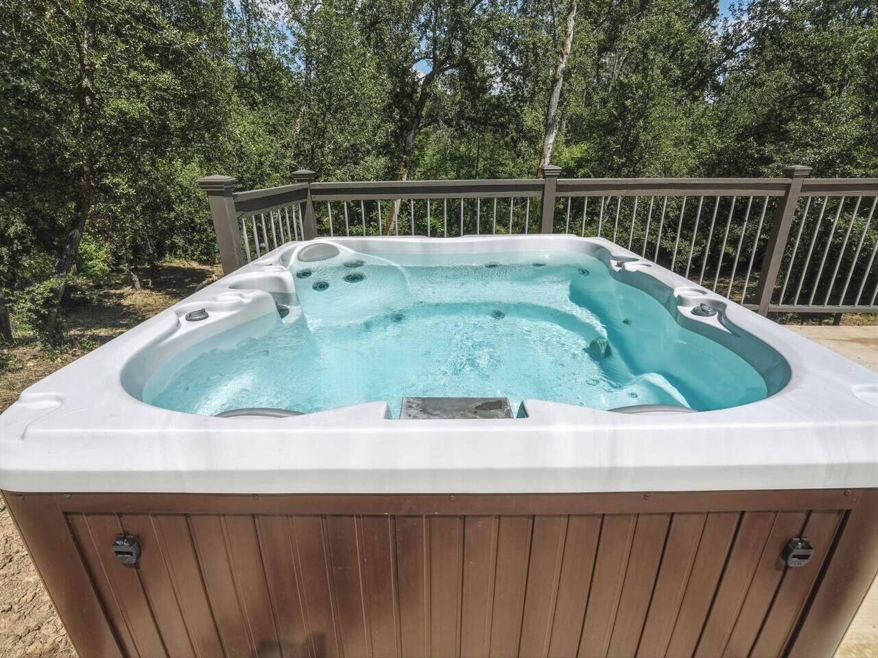 Un bain à remous avec une structure extérieure en bois, entouré d’une terrasse en bois et agrémenté d’une rambarde en métal.