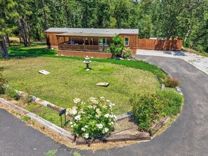 A wooden cabin with a porch, surrounded by a well-maintained lawn and a small garden with white flowers. - Private Creekside Cabin • Hot Tub • Sauna • Views (North Fork)