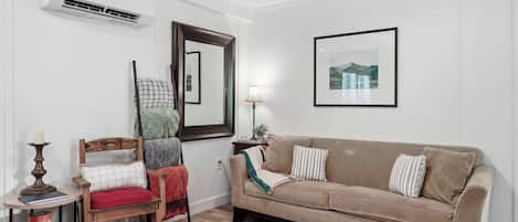 Una sala de estar con un sofá color beige, una silla de madera, una lámpara y un cuadro en la pared.