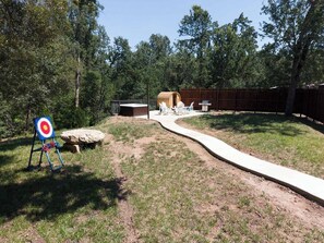 A backyard with a concrete path, a target, and a barrel.