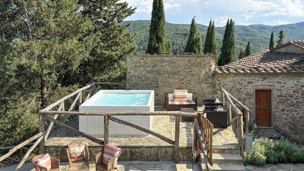 Un bâtiment en pierre doté d’une piscine, de meubles en osier et offrant une vue sur les montagnes.