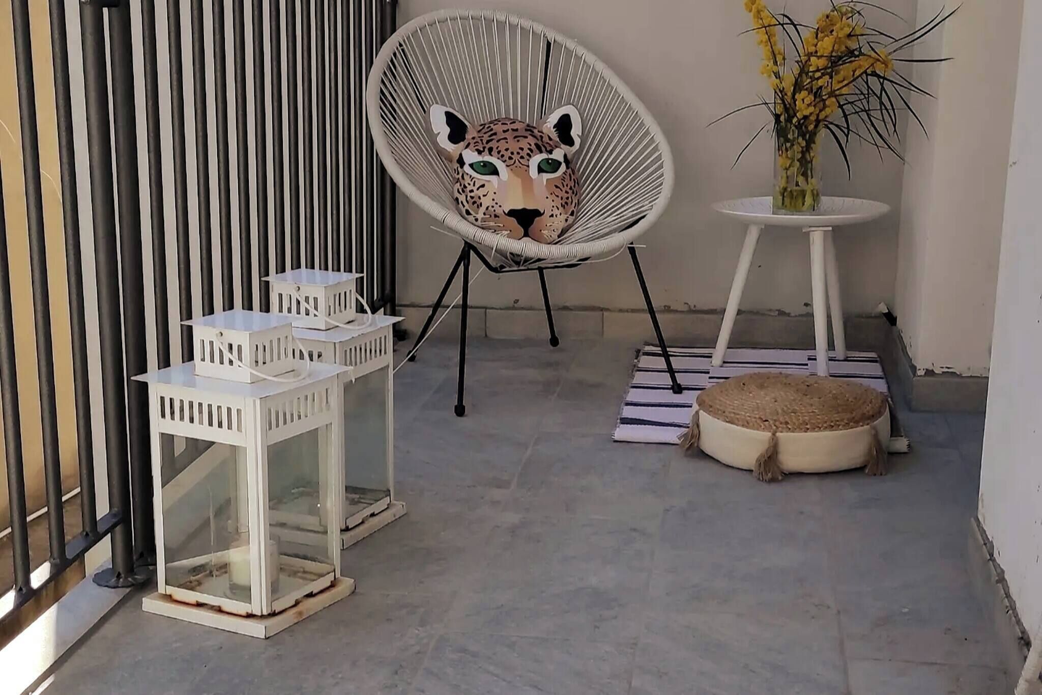 A chair with a leopard face design, a white lantern, and a small table with a vase of flowers.