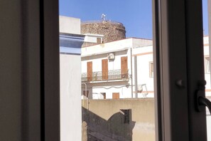 A building with a stone structure on top, a balcony with a metal railing, and a window with a white frame. - The Courtyard by the Seaside (Calasetta)