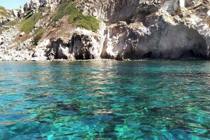 A coastal scene with clear turquoise water, rocky cliffs, and sparse vegetation. - The Courtyard by the Seaside (Calasetta)