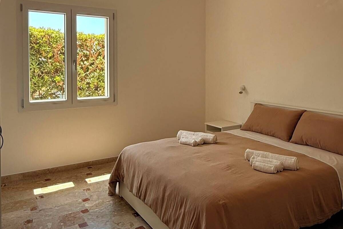 Ein Schlafzimmer mit einem Bett, zwei Fenstern, einer Deckenleuchte und einem Fliesenboden.