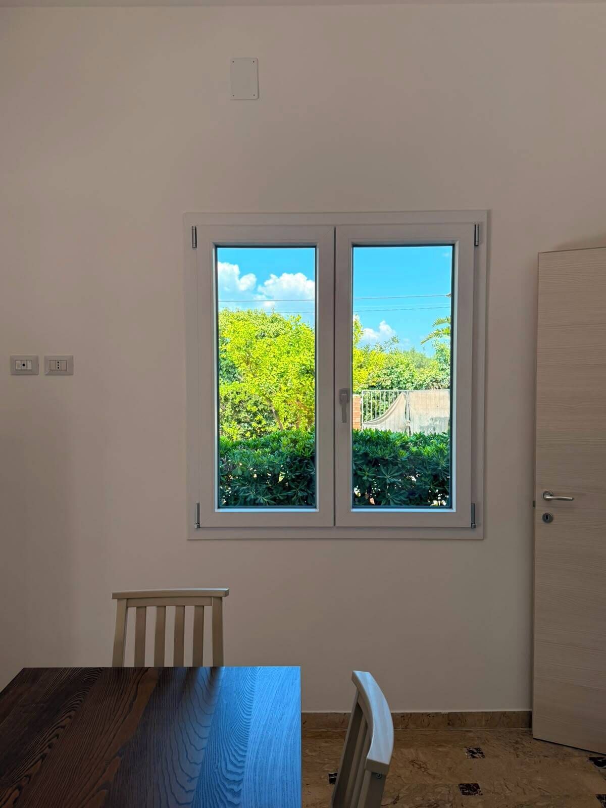 Um quarto com janela, porta e mesa.