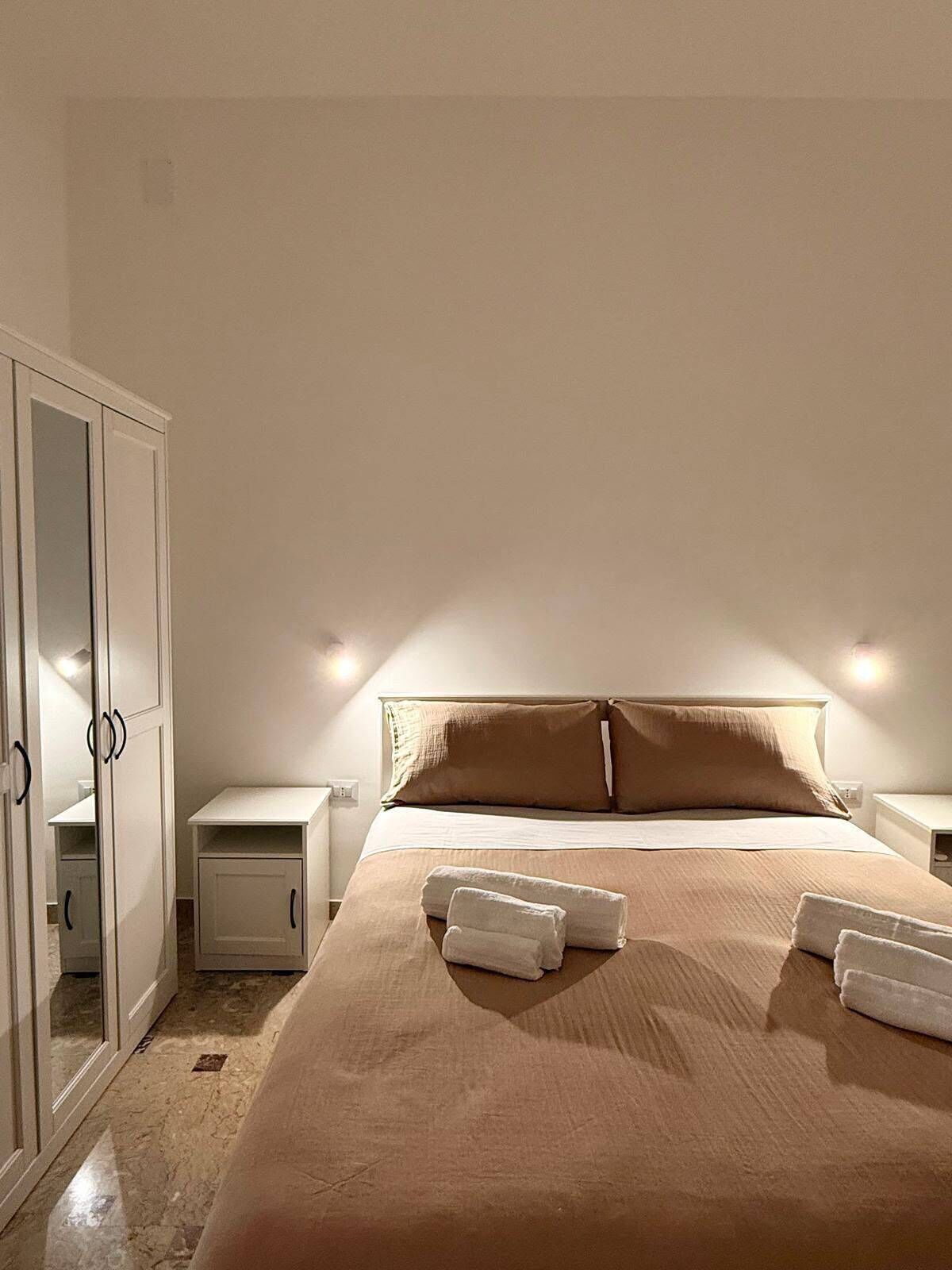 Um quarto com uma cama, mesa de cabeceira, guarda-roupa e espelho.