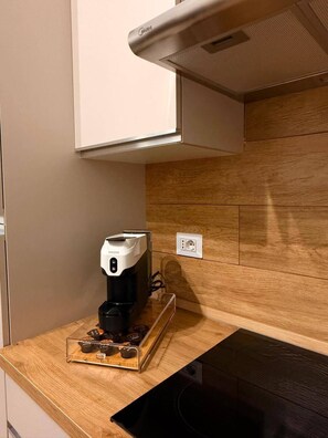 A kitchen with a coffee machine on a wooden countertop, a white cabinet above, and a wooden backsplash. - Casa Volqart (Località Rogana I)