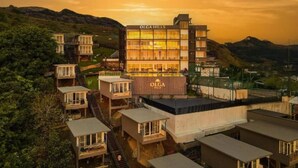 A multi-story hotel with a prominent 'OLGA HILLS' sign, surrounded by lush greenery and hills.