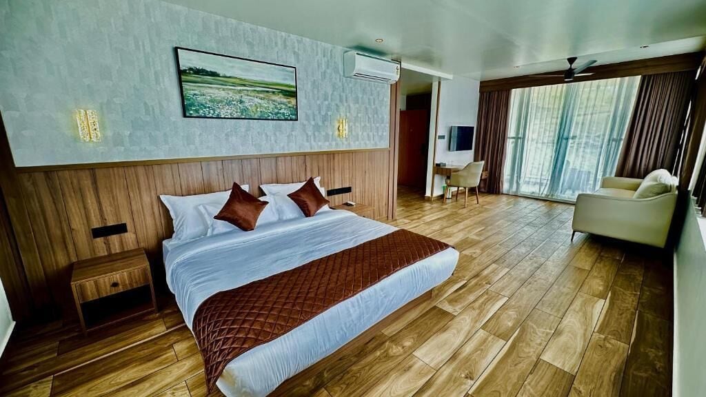 Habitación de hotel con una cama grande, piso de madera, un cuadro en la pared y vistas por la ventana.