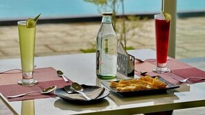 A table with a bottle, a glass, and a plate of food, set against a scenic view.