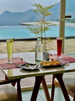 A table with a bottle, a glass, and a plate of food, set against a scenic view.