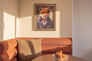 Ein Wohnzimmer mit einer Couch, einem gerahmten Bild an der Wand und einem Tisch mit Obstschale.