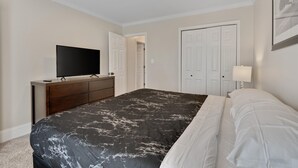 Een slaapkamer met een bed, een kaptafel, een televisie en een deur.