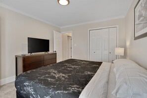 Ein Schlafzimmer mit Bett, Kommode, Fernseher und Tür.