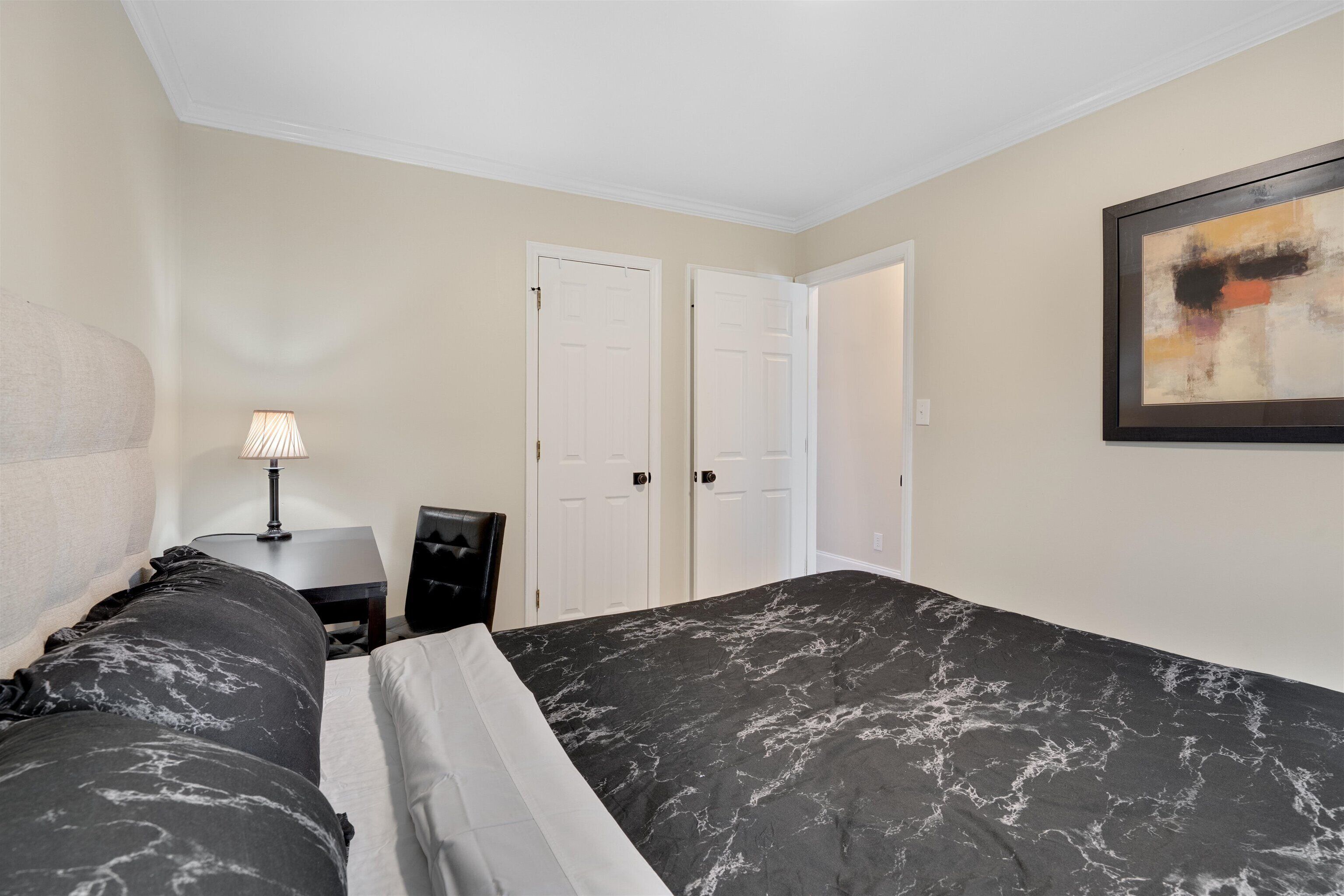 A hotel room with a bed, a desk, a chair, and two doors.