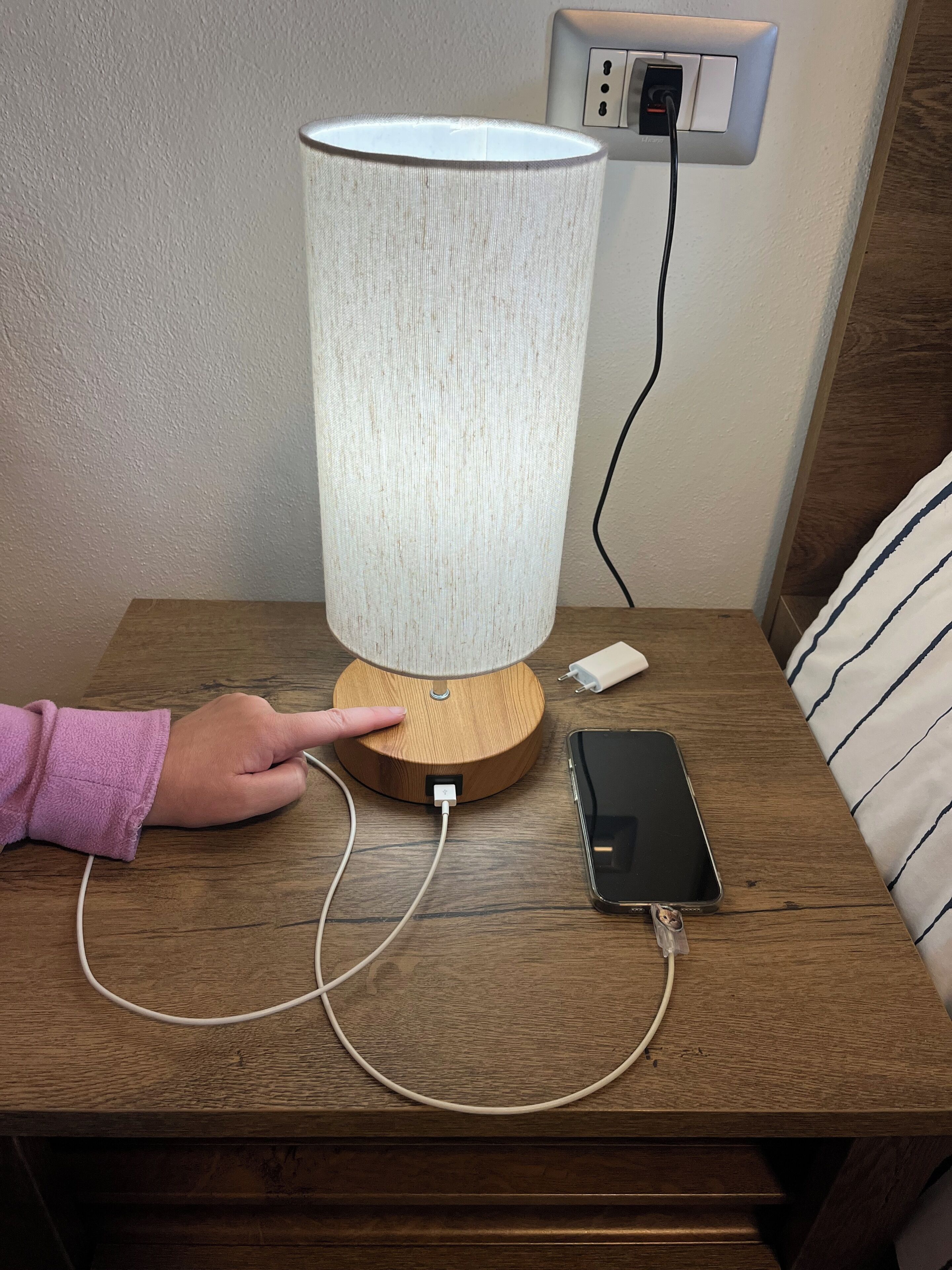 A lamp on a wooden table with a smartphone and charger connected to it.