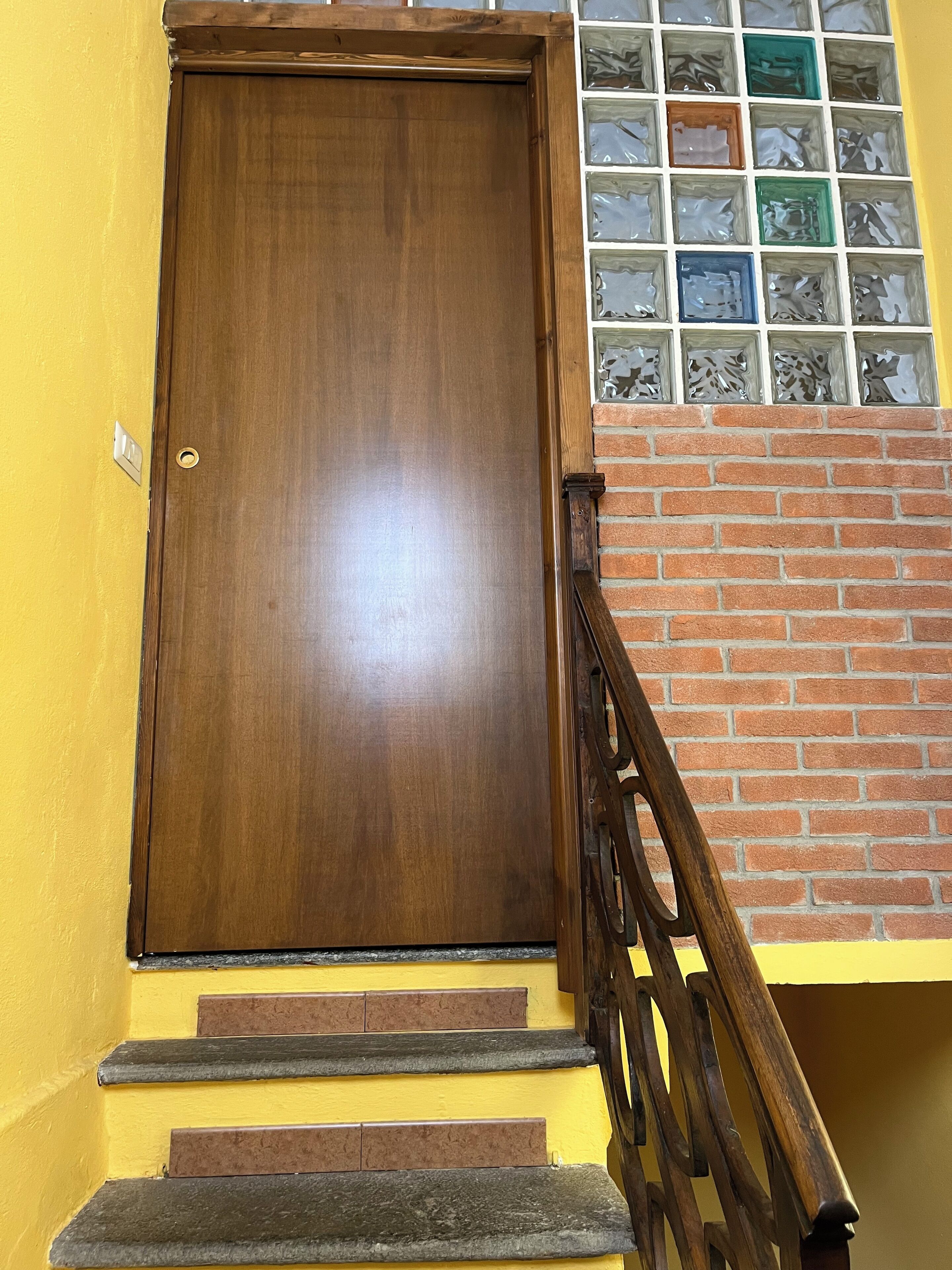 Une porte en bois avec une poignée de porte en laiton, un mur en briques et une fenêtre avec des vitraux colorés.