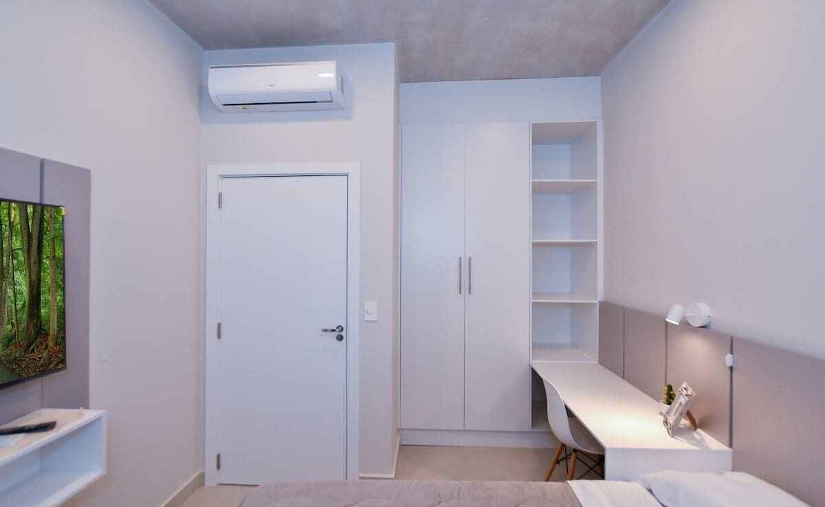 A modern room with a white door, built-in shelving, a desk, and an air conditioning unit.