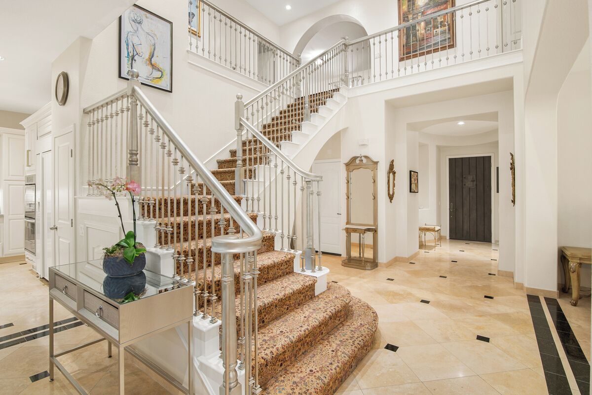 A grand staircase with a glass table and plant, leading to a second floor.