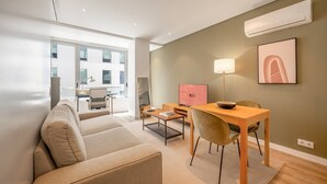 Een moderne woonkamer met een bank, een eettafel met stoelen, een televisie en een lamp.
