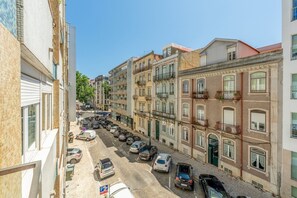 Eine schmale Straße, gesäumt von mehrstöckigen Gebäuden, parkenden Autos und wolkenlosem, blauem Himmel.