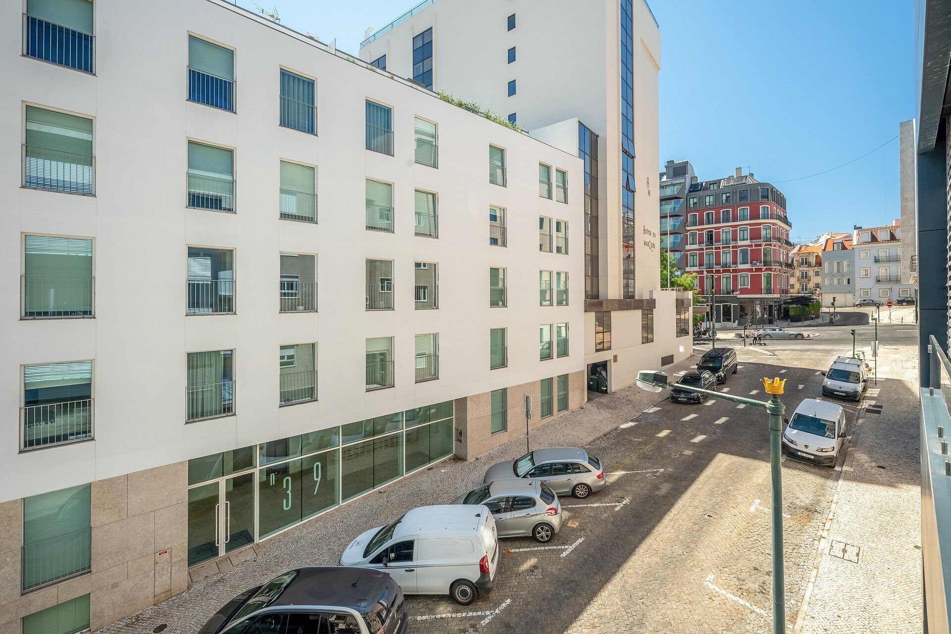 Un edificio de varios pisos con un diseño moderno, con amplias ventanas y un estacionamiento con varios automóviles.