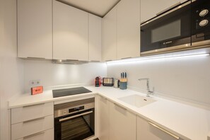 Une cuisine moderne équipée d’un four encastré, d’un four à micro-ondes, d’un évier et d’un plan de travail sur lequel se trouvent un grille-pain et des ustensiles de cuisine.