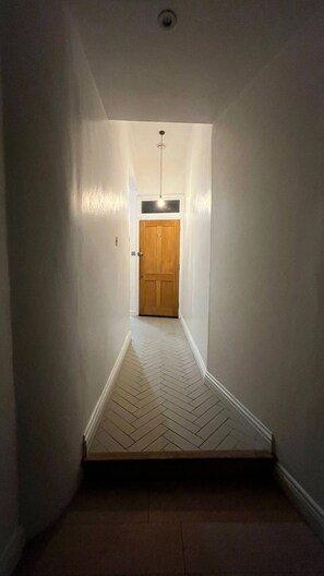 En smal hall med en trädörr längst in, vita väggar och ett golv med fiskbensmönster.