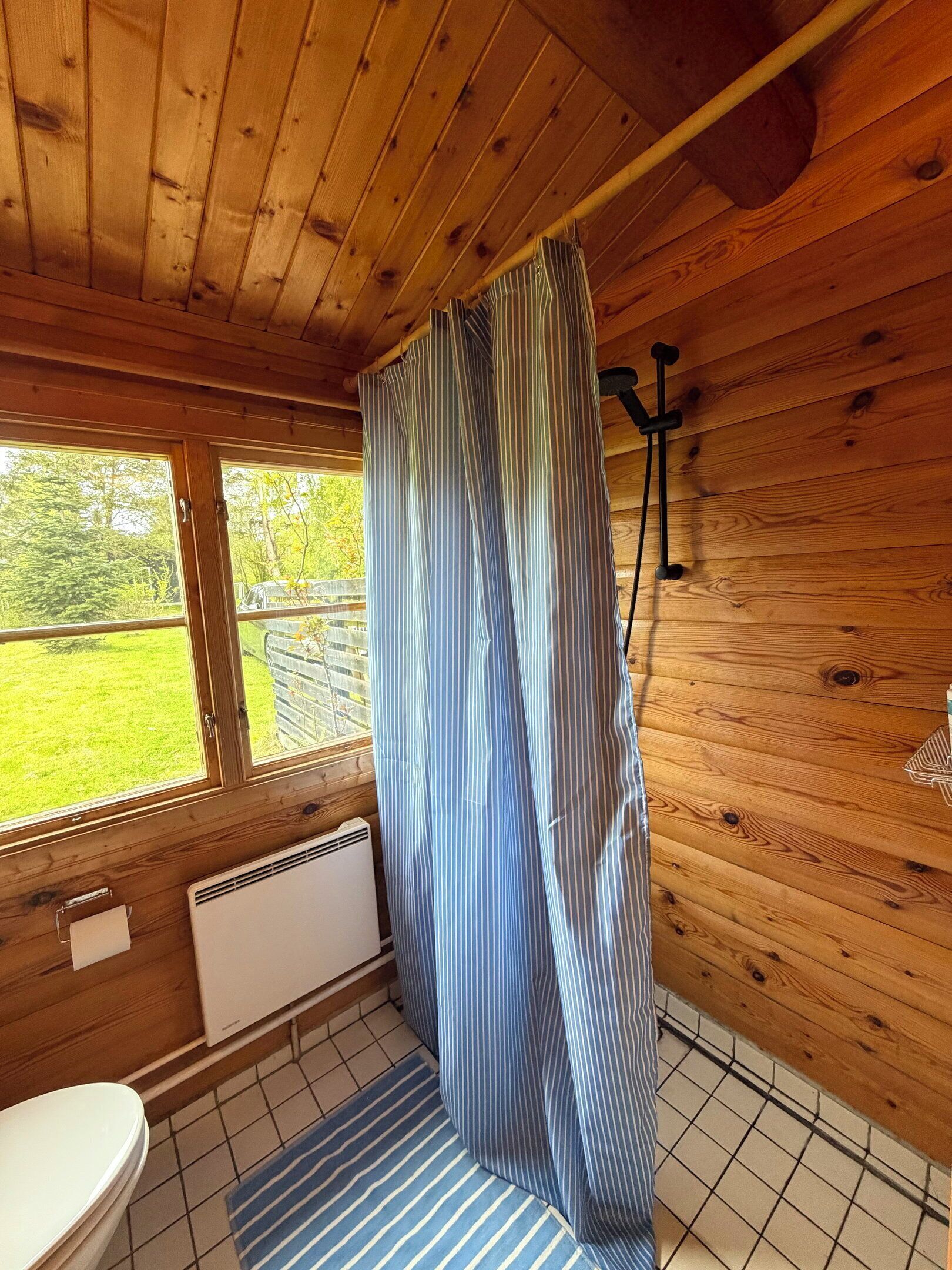 Ein Badezimmer einer Holzhütte mit Toilette, einem Fenster und einem gestreiften Duschvorhang.