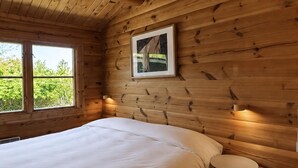 A wooden cabin room with a bed, a small round table, and a framed picture on the wall. - Charming log cabin in Tisvilde (Tisvilde)