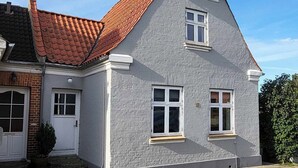 Ein zweigeschossiges Haus mit rotem Ziegeldach, weißen Fensterrahmen und einer grauen Außenwand.